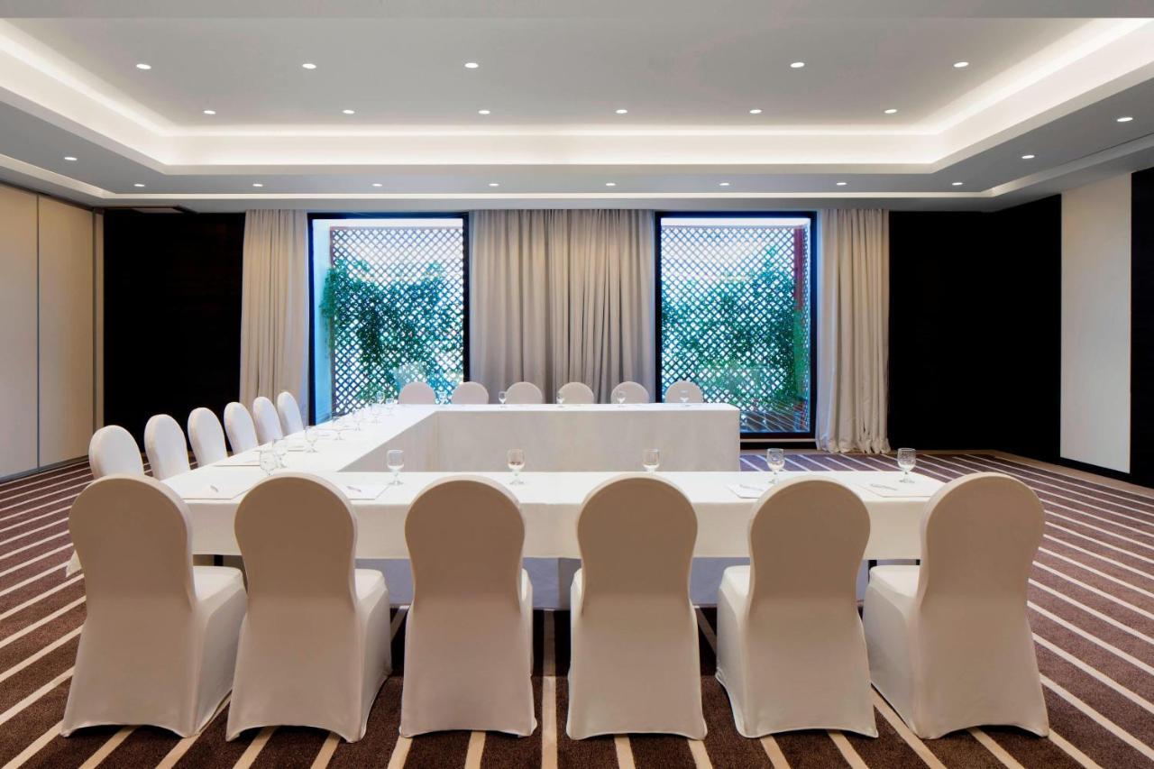 Le Meridien Dubai Hotel & Conference Centre Exterior photo The photo shows a modern conference room designed for meetings or gatherings. It features a long rectangular table covered with a white tablecloth, surrounded by white chairs. The room is well-lit with recessed lighting in the ceiling and has large w