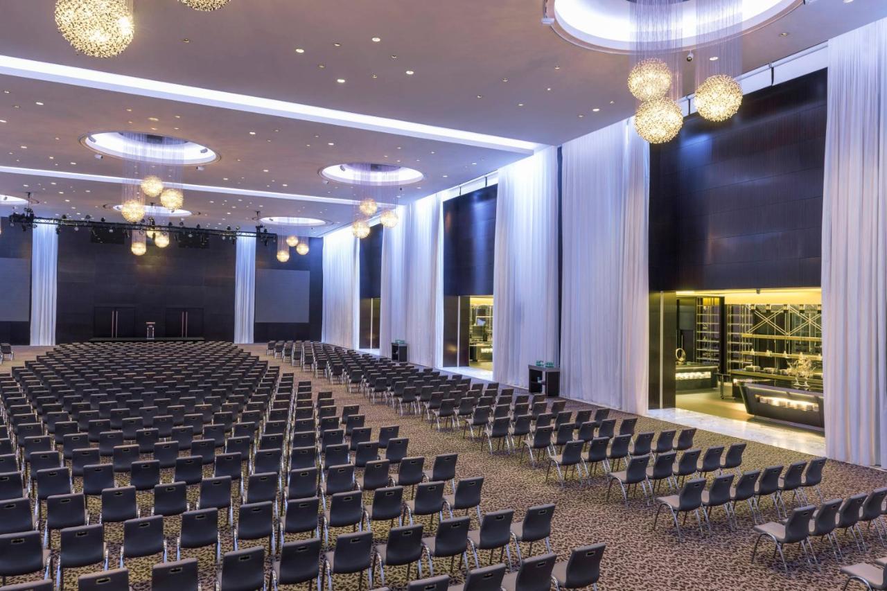 Le Meridien Dubai Hotel & Conference Centre Exterior photo The photo shows a large conference or event hall filled with rows of black chairs arranged in a neat grid formation. The room is well-lit with modern lighting fixtures hanging from the ceiling, and there are soft drapes or panels on the walls. In the