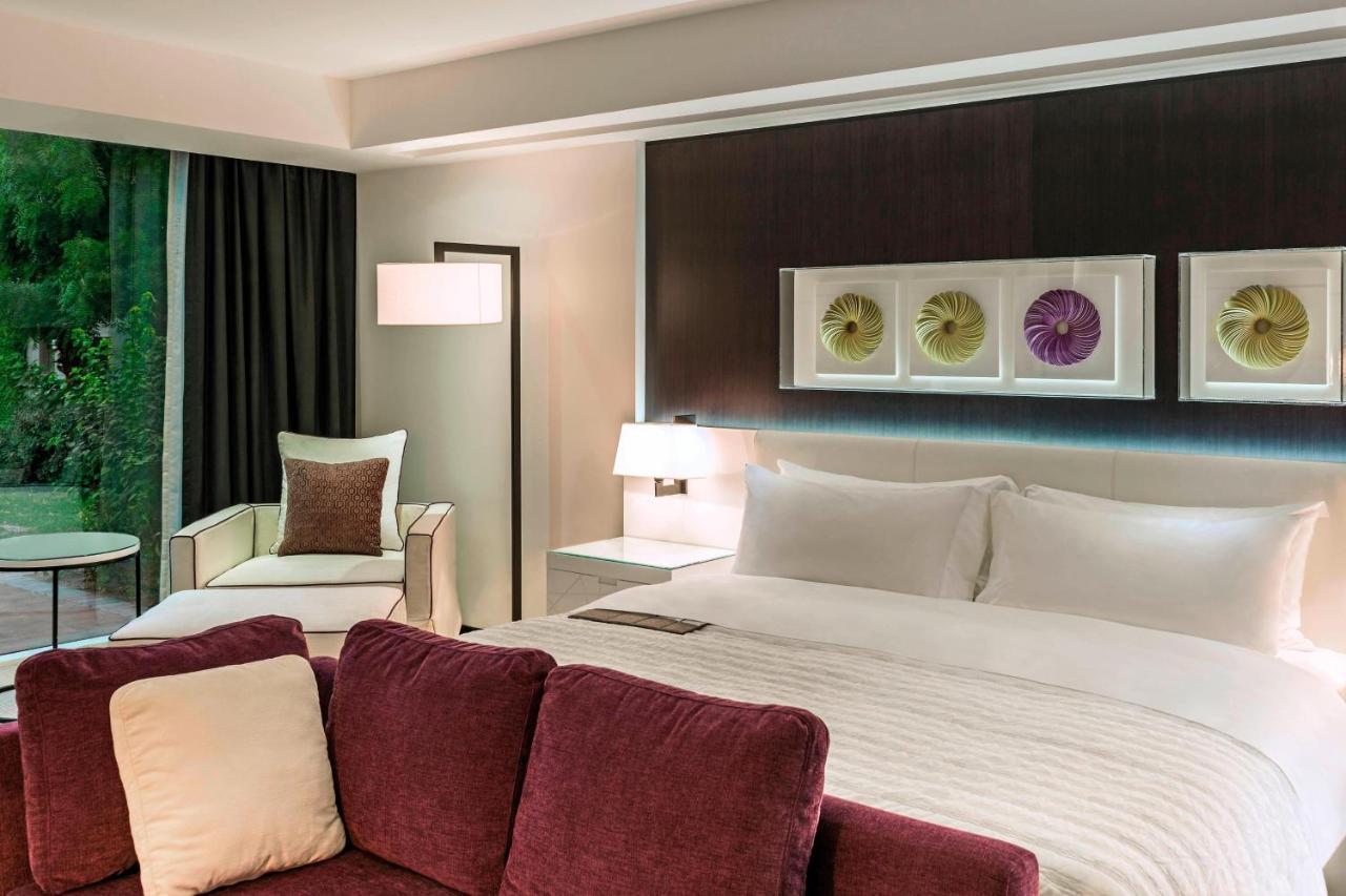Le Meridien Dubai Hotel & Conference Centre Exterior photo The photo depicts a modern hotel room. It features a large bed with white bedding and elegant headboard. To one side, there's a comfortable armchair and a small round table. The room has dark curtains, allowing for a cozy atmosphere, and a decorative