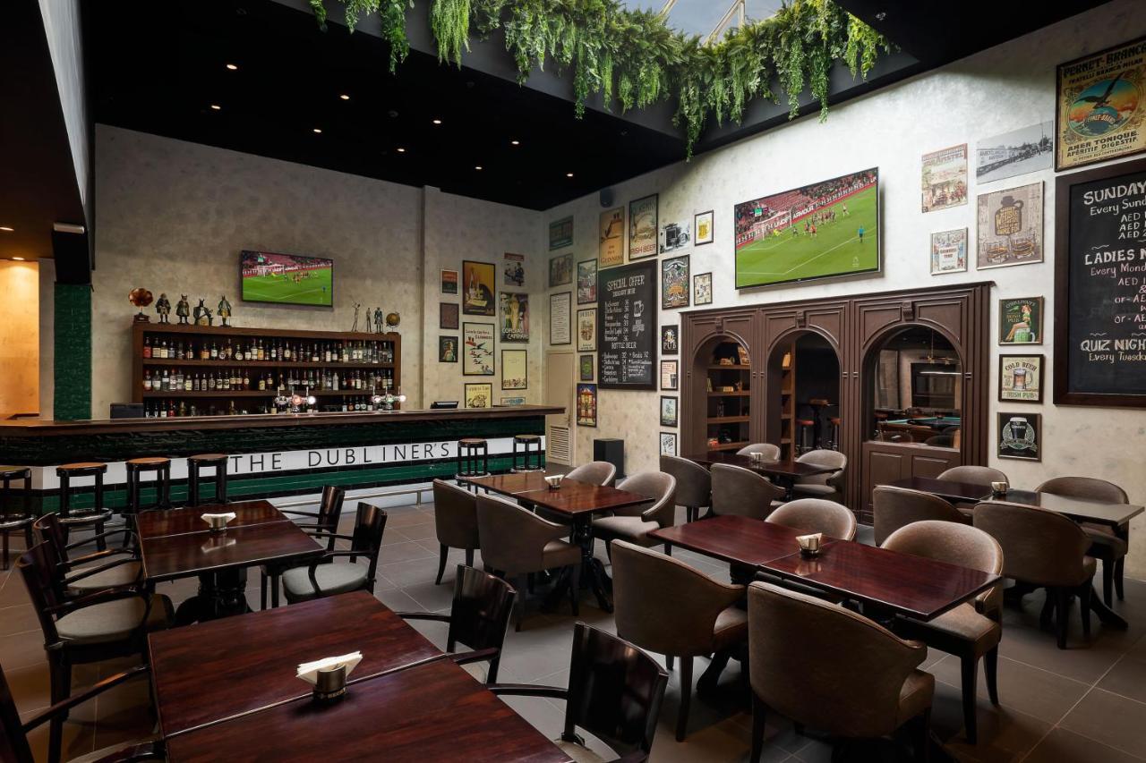 Le Meridien Dubai Hotel & Conference Centre Exterior photo The photo shows the interior of a restaurant or pub. The space features a bar area with a variety of bottles displayed on the shelves behind it. There are several tables arranged in the dining area, and the seating appears comfortable with upholstere