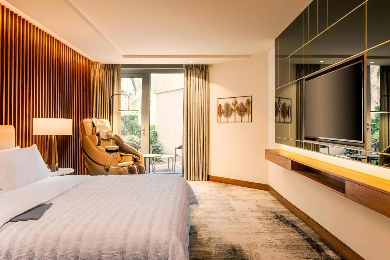 Le Meridien Dubai Hotel & Conference Centre Exterior photo The photo depicts a modern hotel room designed with a contemporary aesthetic. The room features a large bed with crisp white bedding, situated against a backdrop of wooden paneling. There are stylish curtains framing a window that likely leads to a b