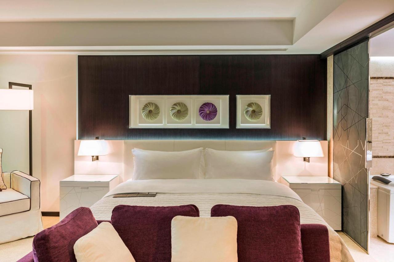 Le Meridien Dubai Hotel & Conference Centre Exterior photo The photo depicts a modern hotel room featuring a large, neatly made bed with white linens and a purple throw. On the wall above the bed, there are three framed artworks displayed, with a decorative element in the center. On either side of the bed, t