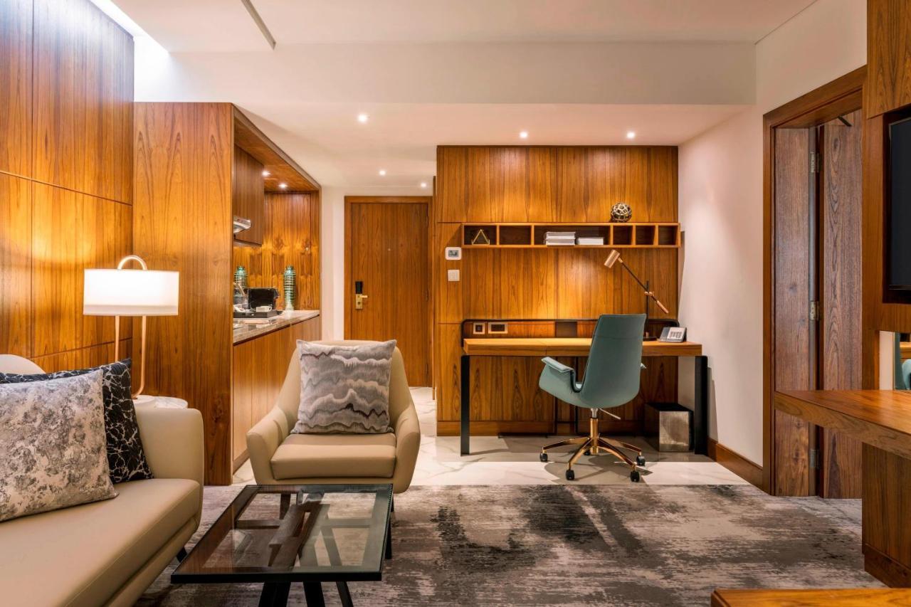 Le Meridien Dubai Hotel & Conference Centre Exterior photo The photo depicts a stylish and modern interior space, likely a hotel room or a living area. The design features wooden paneling on the walls, adding warmth to the atmosphere. On one side, there's a comfortable seating area with a light-colored sofa 