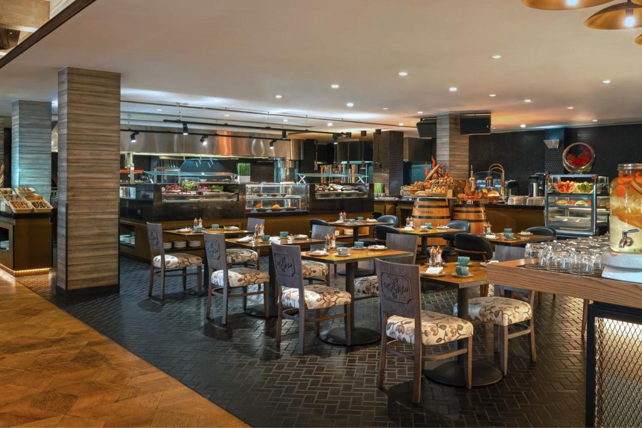 Le Meridien Dubai Hotel & Conference Centre Exterior photo The photo depicts a modern restaurant interior. It features a spacious dining area with several tables and chairs arranged thoughtfully. The tables have floral-patterned upholstery, creating a warm and inviting atmosphere. 

In the background, there 