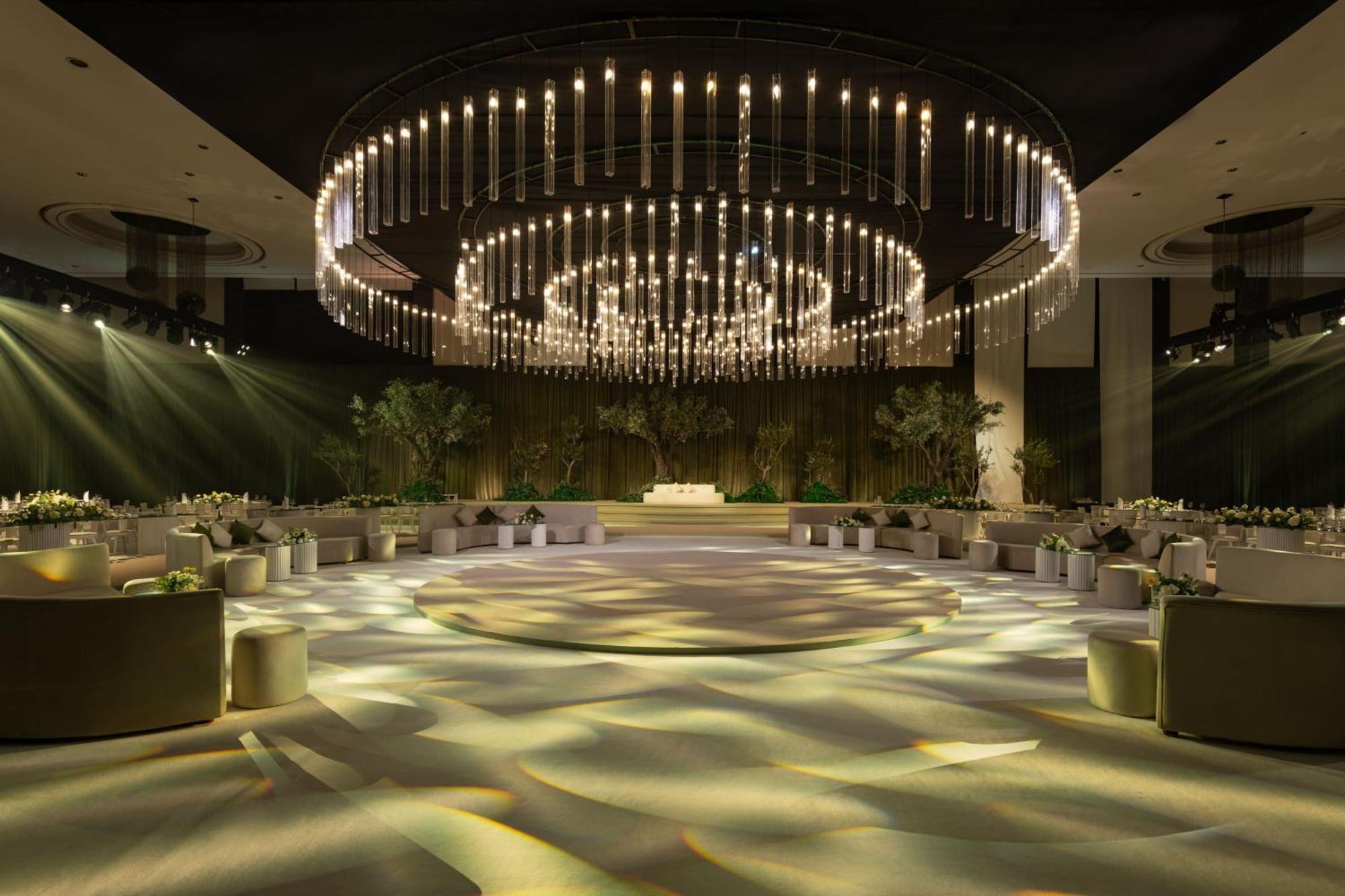 Le Meridien Dubai Hotel & Conference Centre Exterior photo The photo shows an elegantly designed event space with a spacious layout. A large, circular chandelier hangs prominently from the ceiling, adorned with multiple lights that create a dramatic illumination effect. The room is illuminated with soft ligh