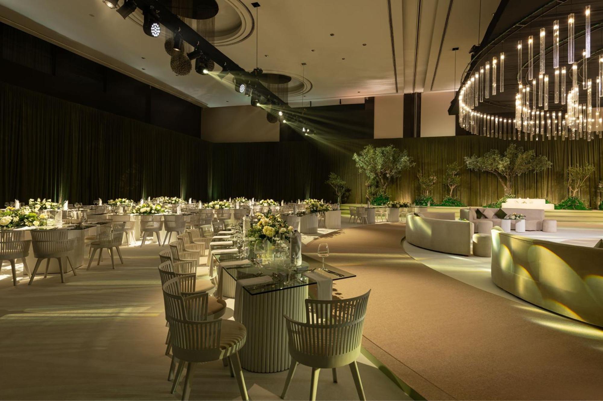 Le Meridien Dubai Hotel & Conference Centre Exterior photo The image depicts a sophisticated indoor event space, likely set up for a formal gathering or celebration. The room features elegantly arranged round tables with white tablecloths, each adorned with floral centerpieces. The lighting is soft and ambie